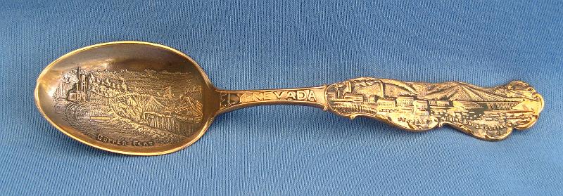 Souvenir Mining Spoon Copper Flat.JPG - SOUVENIR MINING SPOON COPPER FLAT ELY NEVADA - Copper souvenir mining spoon, embossed scene of open pit copper mine in bowl with marking COPPER FLAT at bottom, handle is a skyline depiction of mountains with buildings and smokestacks and a bridge with ELY NEVADA marked on handle, Steptoe Mining and Smelting Co. is marked at the bottom of the skyline, reverse has Paye & Baker makers mark with Sterling x’ed out, 5 1/4 in. long, weight 21 grams [Copper Flat is today a general reference to the area in eastern Nevada where the great copper discoveries were made at the first of the 20th century.  Copper Flat was also small settlement for a short time in this area (now long gone) approximately 6 miles west of Ely, NV in White Pine County.  The Copper Flat area is also associated with several small towns including Kimberly, Riepetown, Ruth and Veteran. The famed open-pit copper mines of eastern Nevada, including the Liberty Pit (largest in the state), are located in this area between Ely and Ruth just south of Highway 50. Through the first half of the 20th century, this area produced nearly a billion dollars in copper, gold and silver. The first mining claims were filed in White Pine County, Nevada, as early as 1867, and the first copper claim was filed in the summer of 1900.  Over the next couple years, an additional 26 claims covering 437 acres of the Copper Flat area were filed.  The Nevada Consolidated Copper Company was organized and incorporated under the laws of Maine on November 17, 1904 to buy up and operate these claims. By May 1906, the company was controlled by the Guggenheim family and their associates and in 1907, steam shovels began stripping the overburden above the Eureka mine to start the open pit mining operations.  In 1906, the Nevada Consolidated Copper Company and the Cumberland and Ely Mining Corporation formed a partnership to build a smelter in the area to process the ores from Copper Flat.  Named the Steptoe Valley Mining and Smelting Company, the smelter started construction in December 1906 at the small town of McGill some 12 miles north of Ely.  The smelter was completed and operations began on May 15, 1908.  The first copper was shipped from the smelter on August 7 of the same year. Kennecott Utah Copper acquired Nevada Consolidated Copper Company, which included Steptoe Valley Mining and Smelting Company and the smelter at McGill, in 1932. In 1983, the price of copper along with the low grade ore being mined led to Kennecott closing the smelter and demolishing it.]